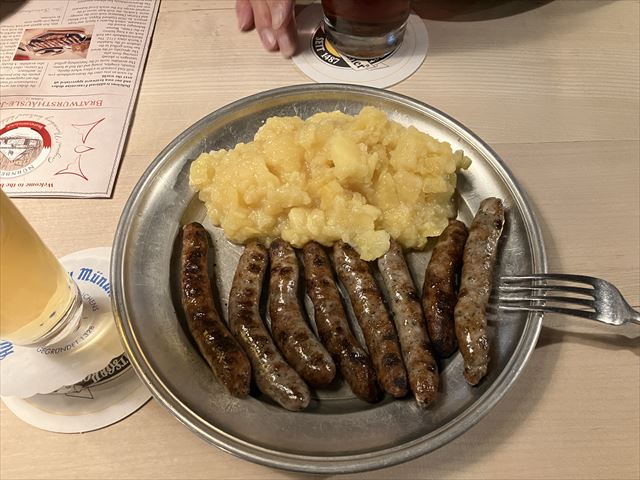 左側にビール、銀色のお皿にマッシュポテトと焼き目のついたソーセージが7本乗っている。